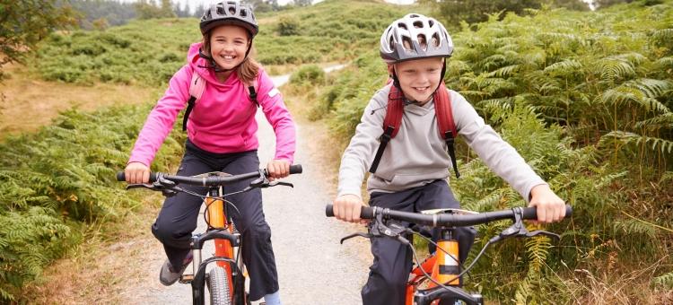 En pige og en dreng på mountainbike med taske på ryggen og cykelhjelm på hovedet.